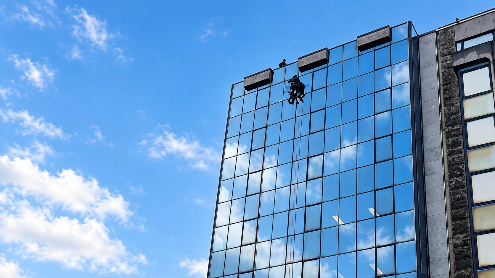 Cordistes nettoyant une façade vitrée sous un ciel bleu